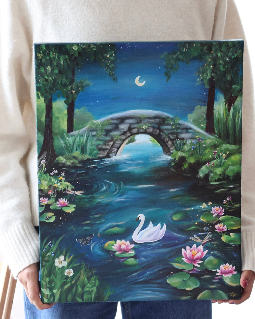 Person holding a painting of a swan on a pond with a bridge and moonlit sky.