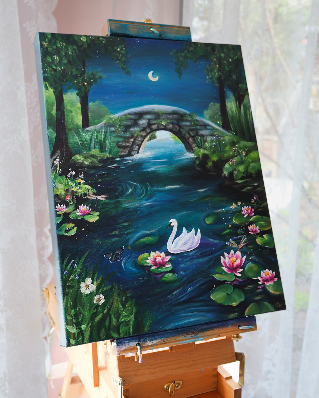 Painting of a serene landscape with a bridge, swan, and lilies on an easel.