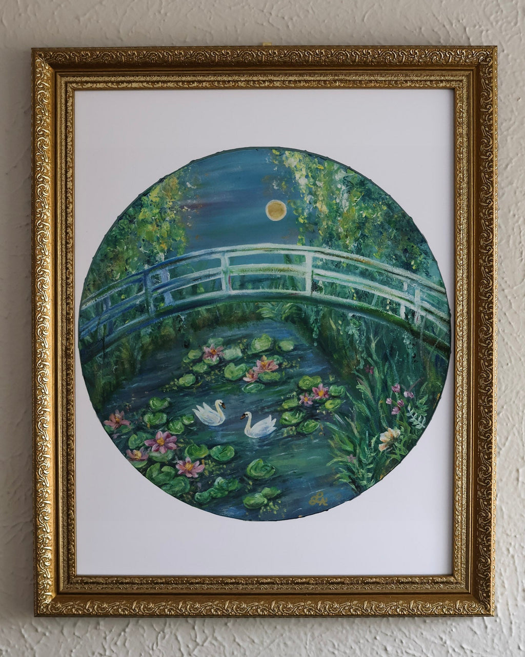 Framed artwork of a bridge over a pond with swans on a white wall.