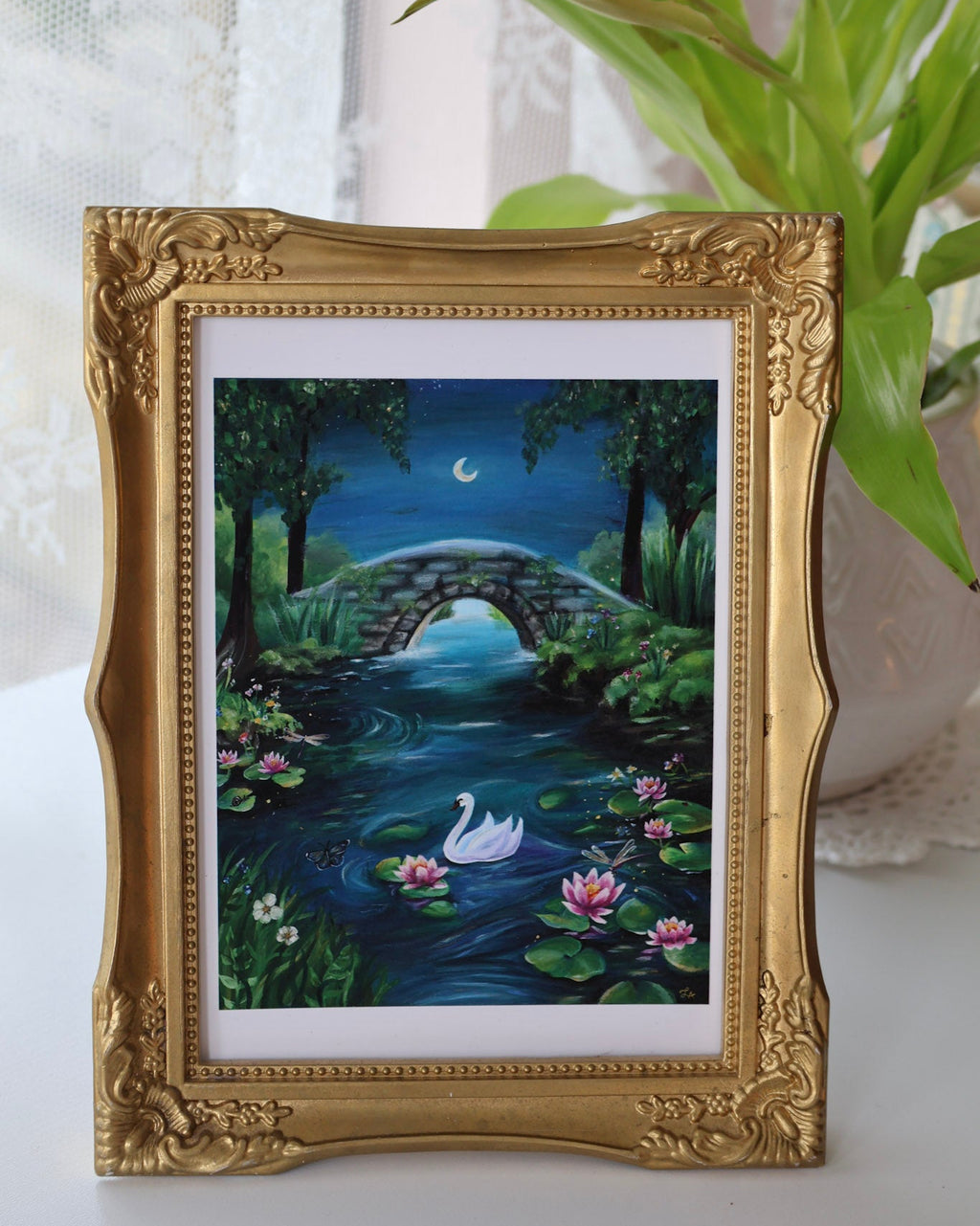 Framed artwork of a swan on a pond with a gold frame.