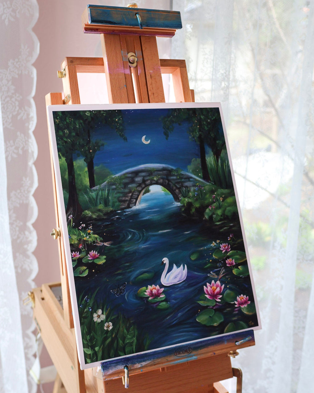 Painting of a swan on a pond with a bridge on an easel against a white curtain.