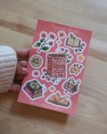 Sticker sheet with book-themed designs held by a person on a wooden surface