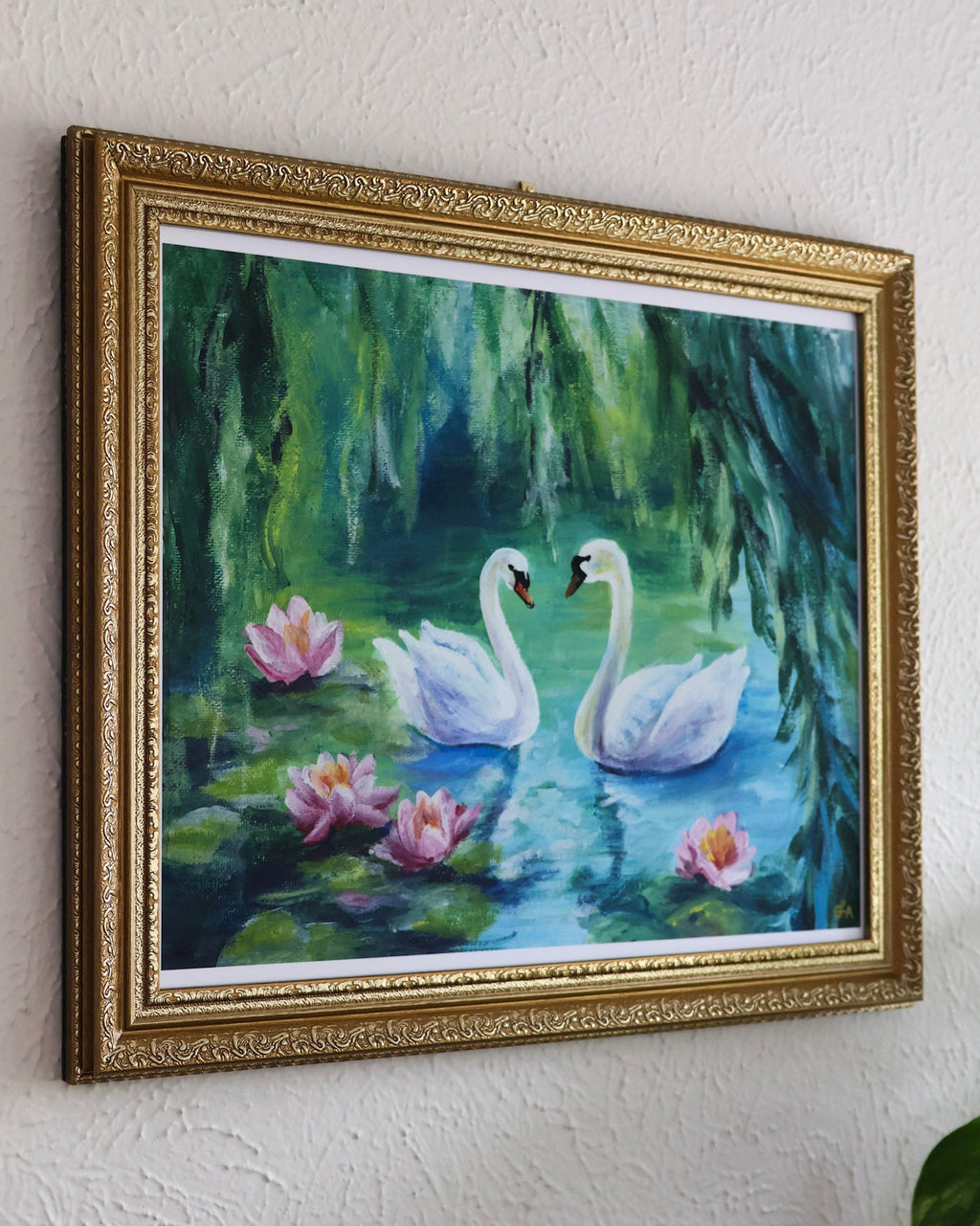 Framed painting of two swans on a pond with lilies on a white wall.
