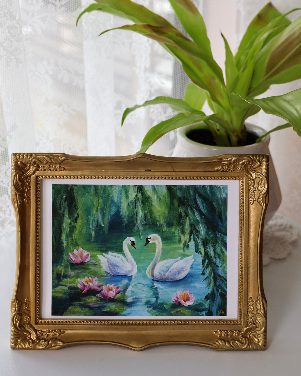 Framed painting of swans on water with a plant in the background